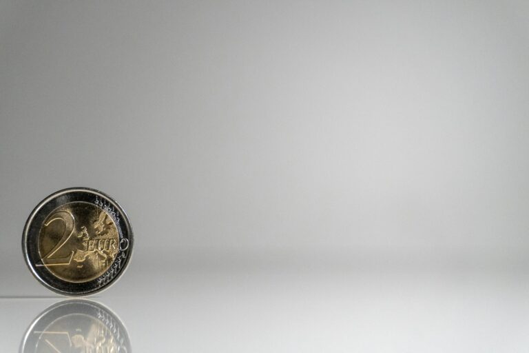 A single 2 Euro coin standing on a reflective surface against a plain background.