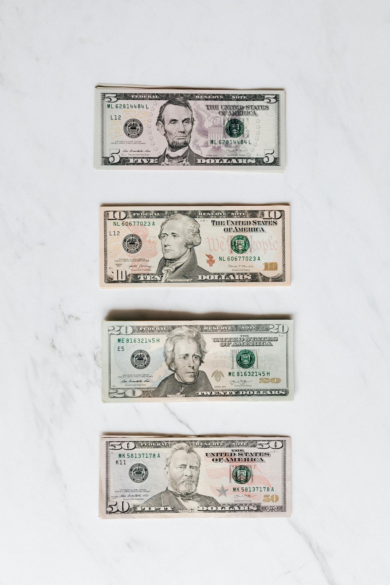 A neat flat lay of US dollar bills on a white marble surface, symbolizing finance and currency.