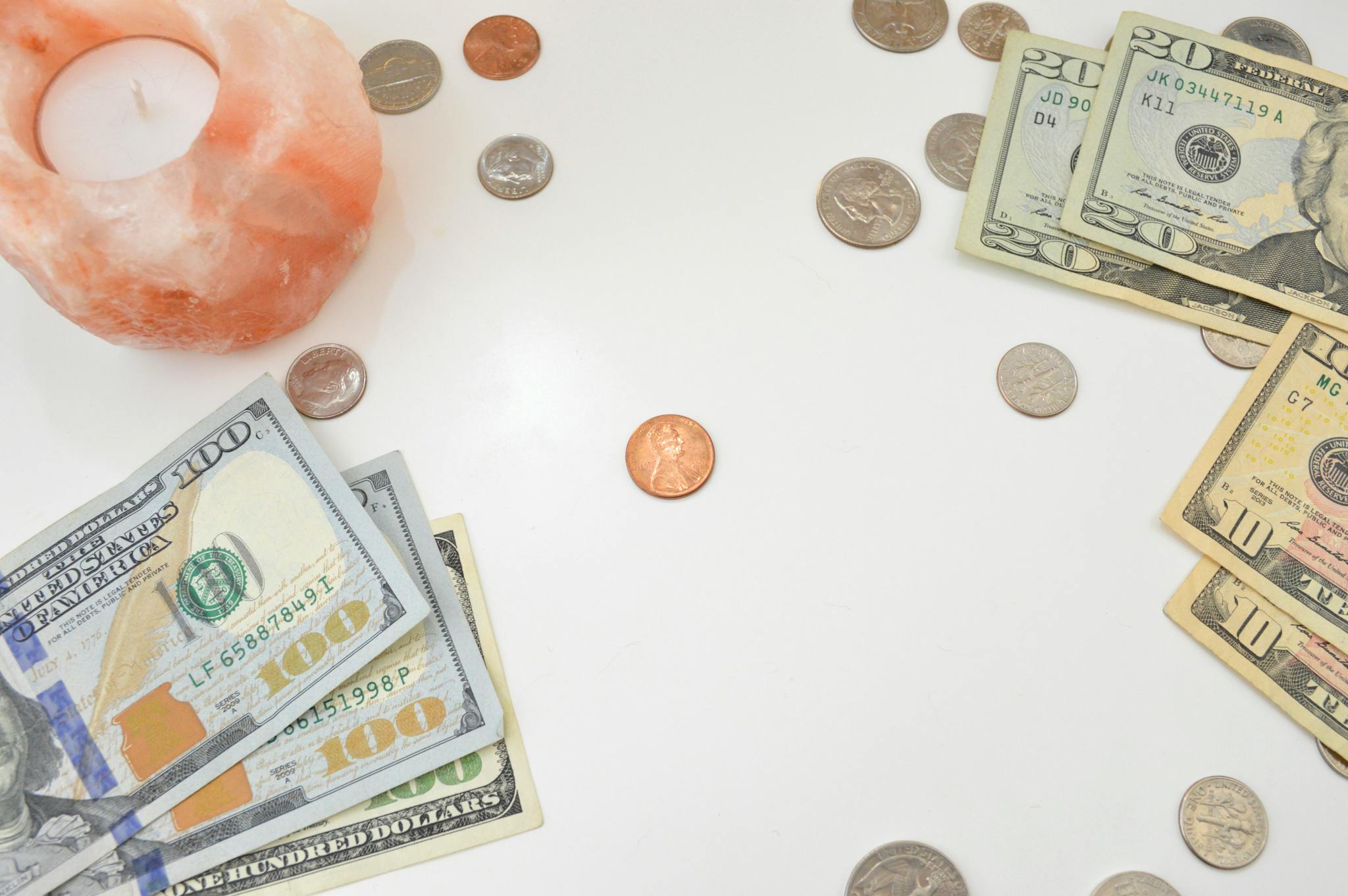Flat lay image featuring US bills, coins, and a candle on a white background, ideal for financial themes.